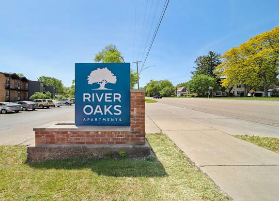 A sign for River Oaks Apartments is displayed in front of a parking lot.