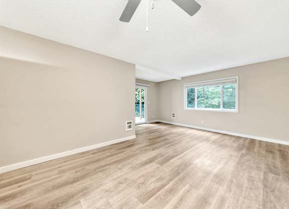A room with a ceiling fan and light, hardwood floors, and a window with a view of trees. at River Lofts Apartments, Tualatin, Oregon