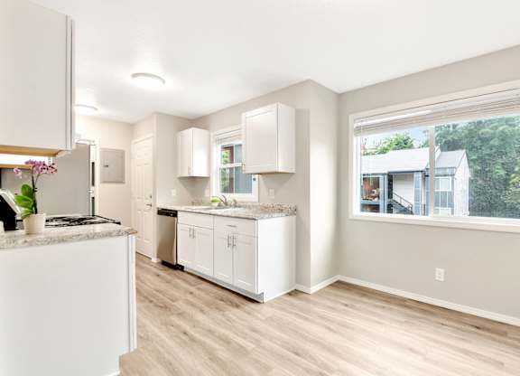 A kitchen with white cabinets and a window overlooking a house. at River Lofts Apartments, Oregon