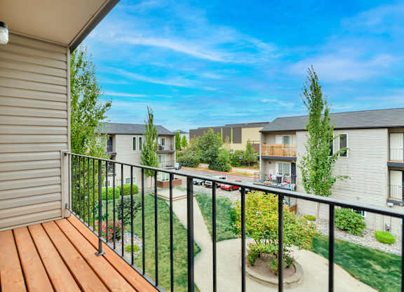 A balcony with a wooden floor overlooks a courtyard with a small tree and a building in the background. at River Lofts Apartments, Oregon