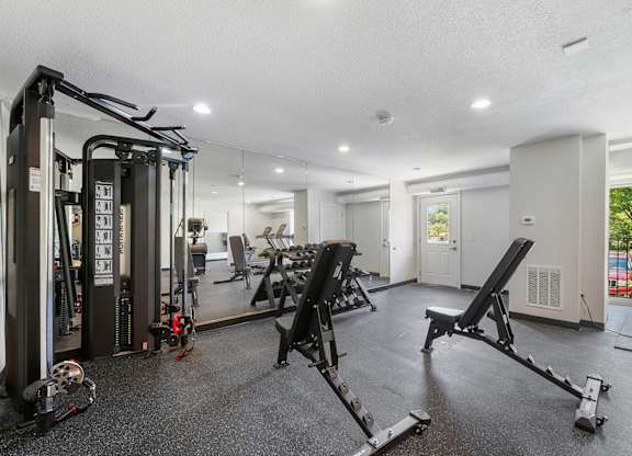 A gym with a variety of equipment including a squat rack, a leg press machine, and a bench press.