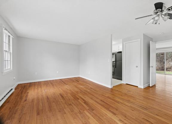 A room with a ceiling fan, wooden floors and white walls.