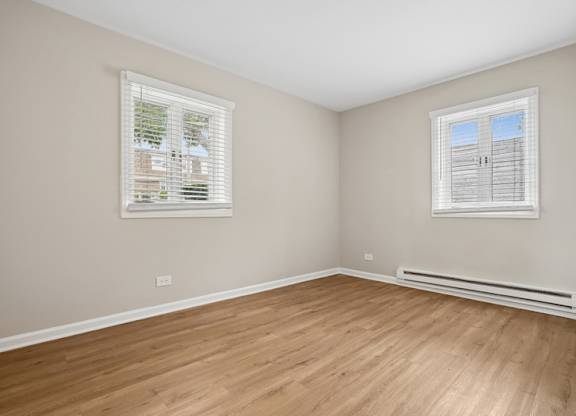 A bedroom with wooden floors and two windows.