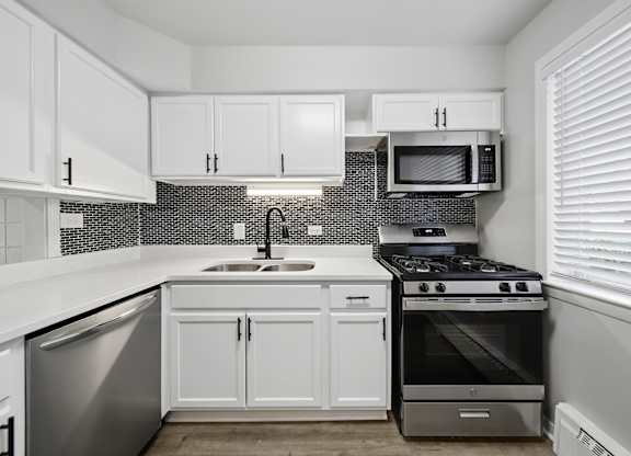 A kitchen with white cabinets and a black and white tiled backsplash.
