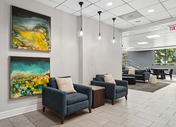 A living room with two blue couches and two paintings on the wall.