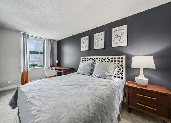 A bedroom with a large bed, a nightstand with a lamp, and three framed pictures on the wall.