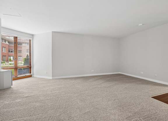 A large empty room with a carpeted floor and a window with blinds.