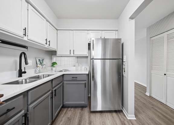 A modern kitchen with a stainless steel refrigerator and wooden flooring.