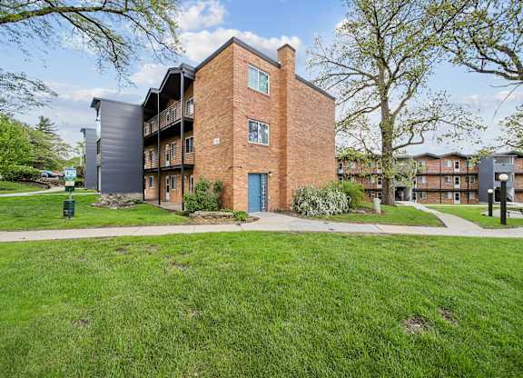 A large brick building with a blue door is surrounded by a grassy area and other buildings.