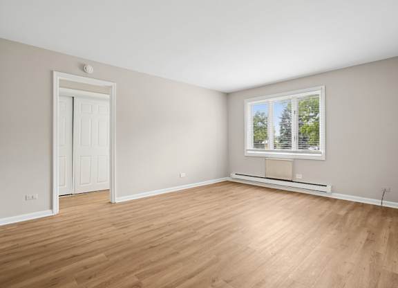 A room with a white door and a window with a view of trees.