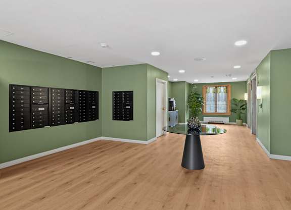 A room with green walls and wooden floors has a black table in the middle.