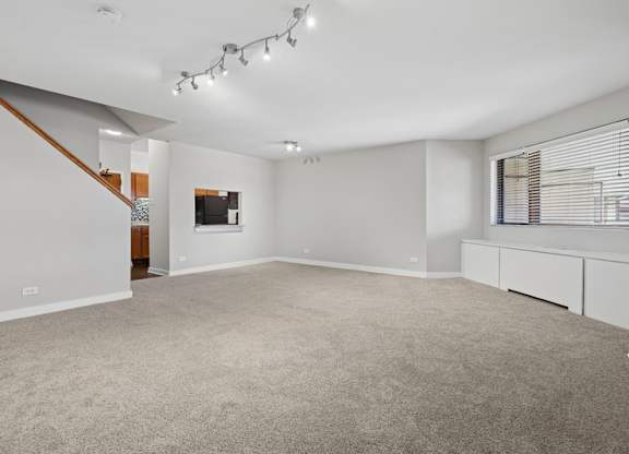 A spacious room with a carpeted floor and a staircase on the left side.