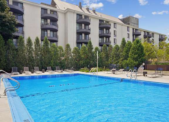 A swimming pool in front of a building with trees in the background.