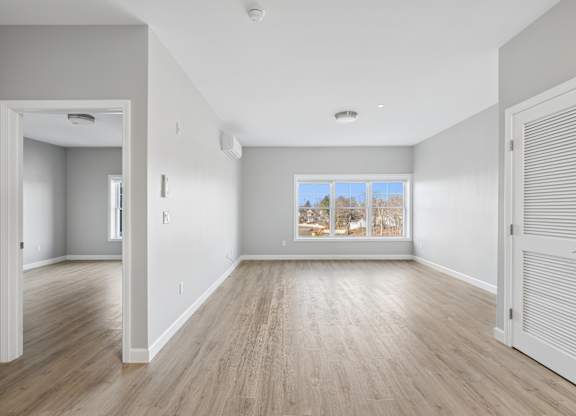 A room with wooden floors and a large window with a view of trees outside.