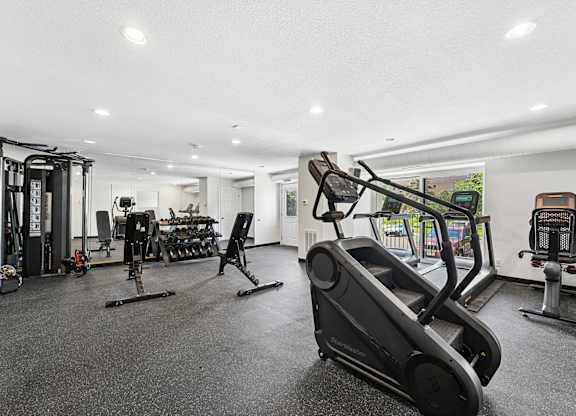 A black treadmill is in the foreground of a well-equipped gym.