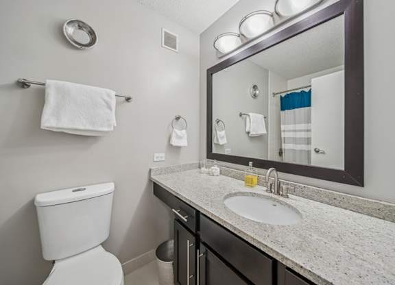A bathroom with a toilet, sink, mirror, and towel rack.