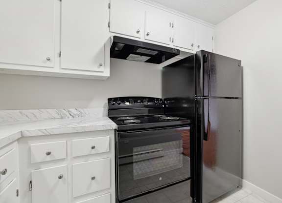 A white refrigerator is in a kitchen with white cabinets and a microwave.
