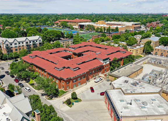 A large red building with a red roof is surrounded by trees and other buildings.