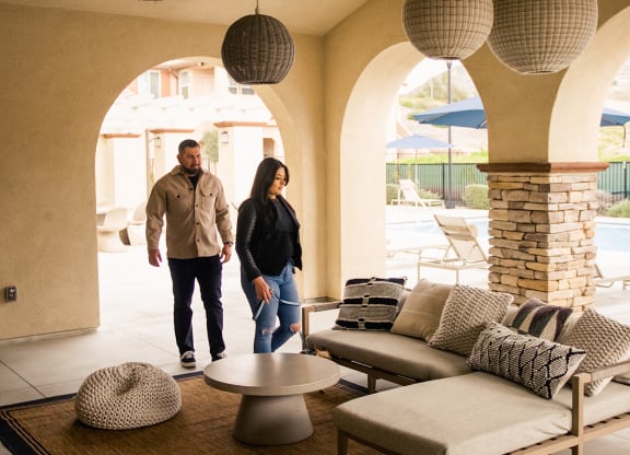 a couple walks through a living room with couches and lamps