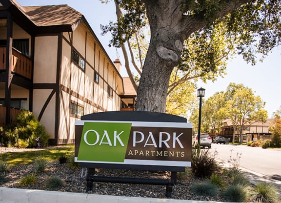 a sign for oak park apartments in front of a tree at Oak Park Apartments, Solvang, CA