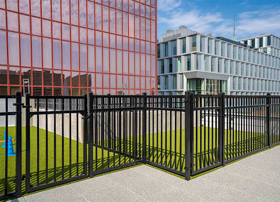 A black metal fence with a green lawn in front of a red building. at Sora Apartments, Minneapolis, MN, 55415