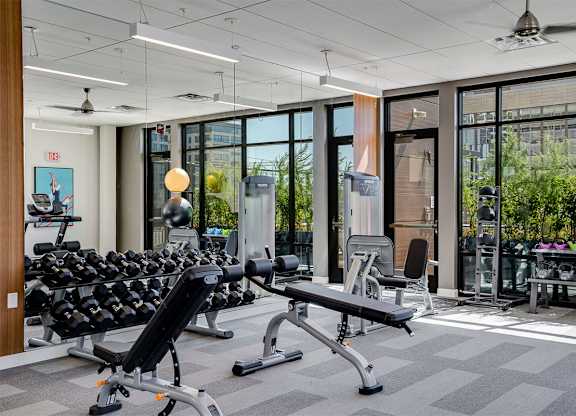 A gym with a variety of equipment including dumbbells, weight machines, and a bench press. at Sora Apartments, Minneapolis, MN