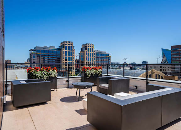 A rooftop patio with a table and chairs overlooking a city skyline at Sora Apartments, Minneapolis 55415