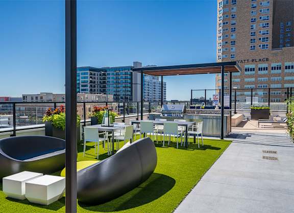 A modern outdoor seating area with a curved bench and a table with chairs. at Sora Apartments, Minneapolis