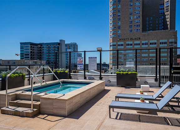 A pool on a rooftop with lounge chairs and a building in the background at Sora Apartments, Minnesota