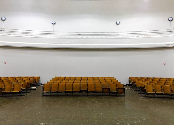 an empty auditorium with yellow seats and a white wall