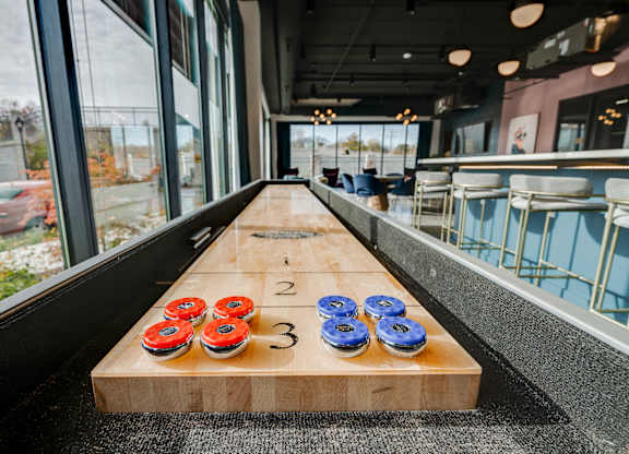 A tabletop shuffleboard indoor next to seating and a large window at The Shale, Minneapolis, MN