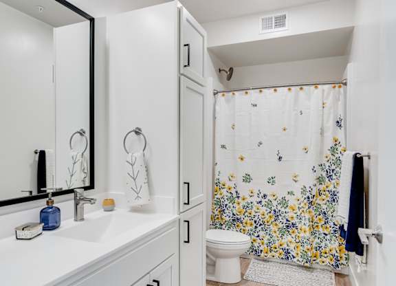 A white bathroom with a floral shower curtain. at The Shale, Minneapolis, MN