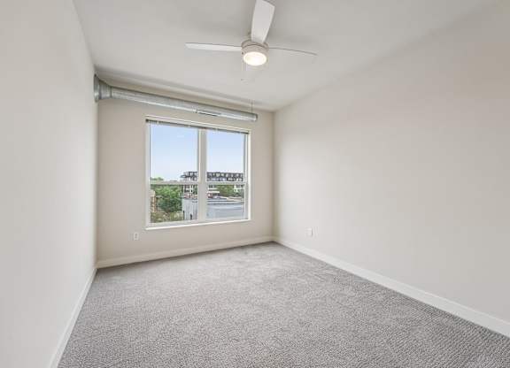 A room with a ceiling fan and a window overlooking a street.