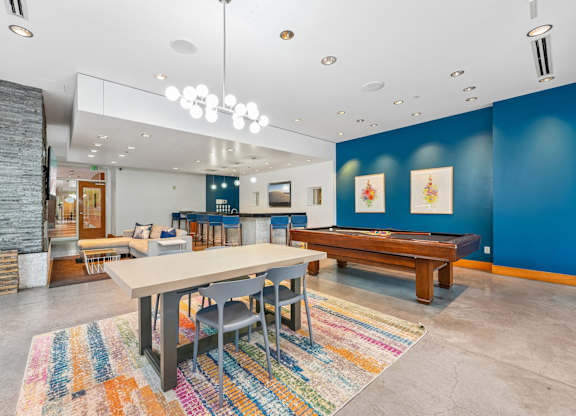A room with a long table and chairs, a stone fireplace, and a colorful rug.