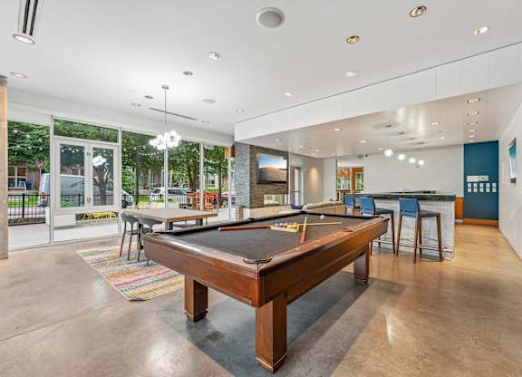 A pool table is in the middle of a room with a bar and a television.