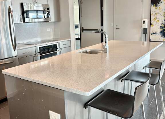 A kitchen with a white counter top and black chairs.