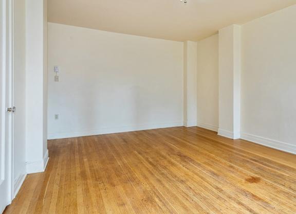 Empty room with wooden flooring and white walls.