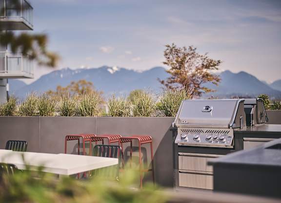 A barbecue grill is on a patio with a table and chairs.