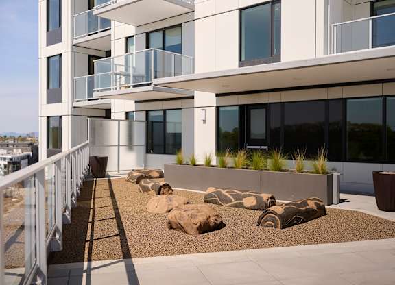 A modern building with a balcony and a landscaped area in front.