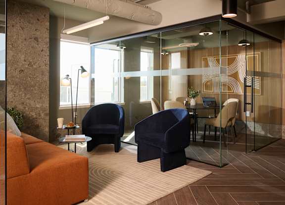 A modern office space with glass walls and a mix of blue and orange furniture.