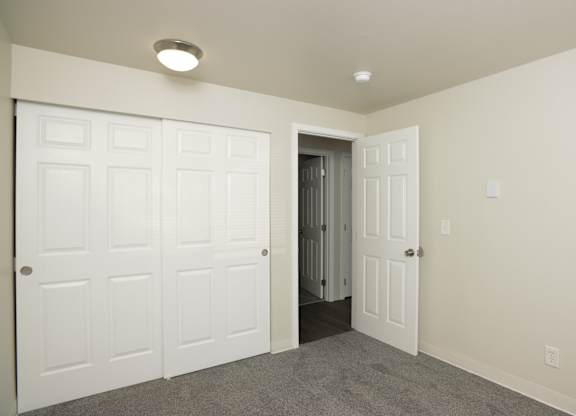 A room with a white door and a grey carpet.