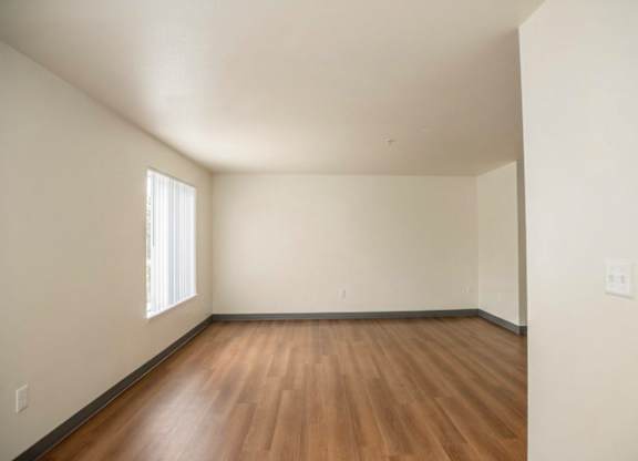 A room with wooden flooring and a window on the left side.