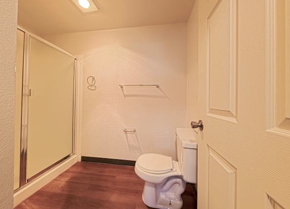 A white toilet with a white tank sits in a bathroom with a wooden floor.