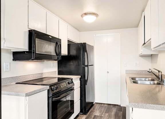 A black refrigerator sits in a kitchen with white cabinets and a stainless steel sink.