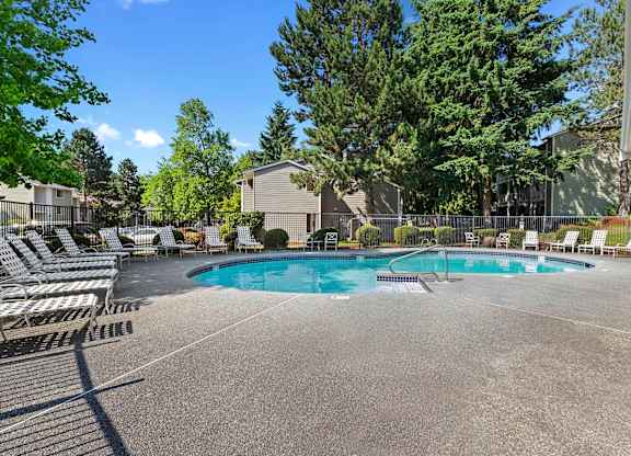 A large outdoor swimming pool surrounded by lounge chairs and trees.