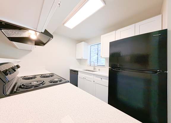 A kitchen with a black refrigerator, white countertop, and a stove with four burners.