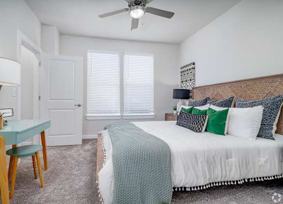 A bedroom with a bed, a table with a lamp, and a ceiling fan.