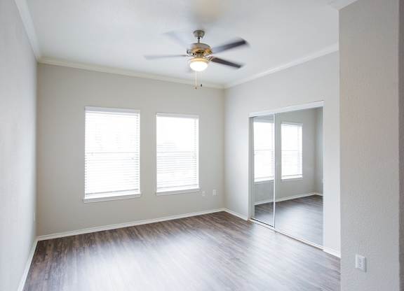 A room with a ceiling fan and three windows.