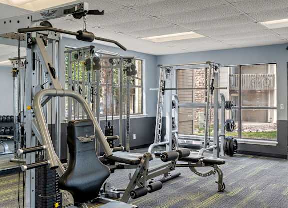 A gym with a variety of equipment including a weight bench, a cable machine, and a squat rack.