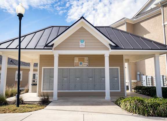 A small building with a brown roof and tan walls has a sign on the front that says